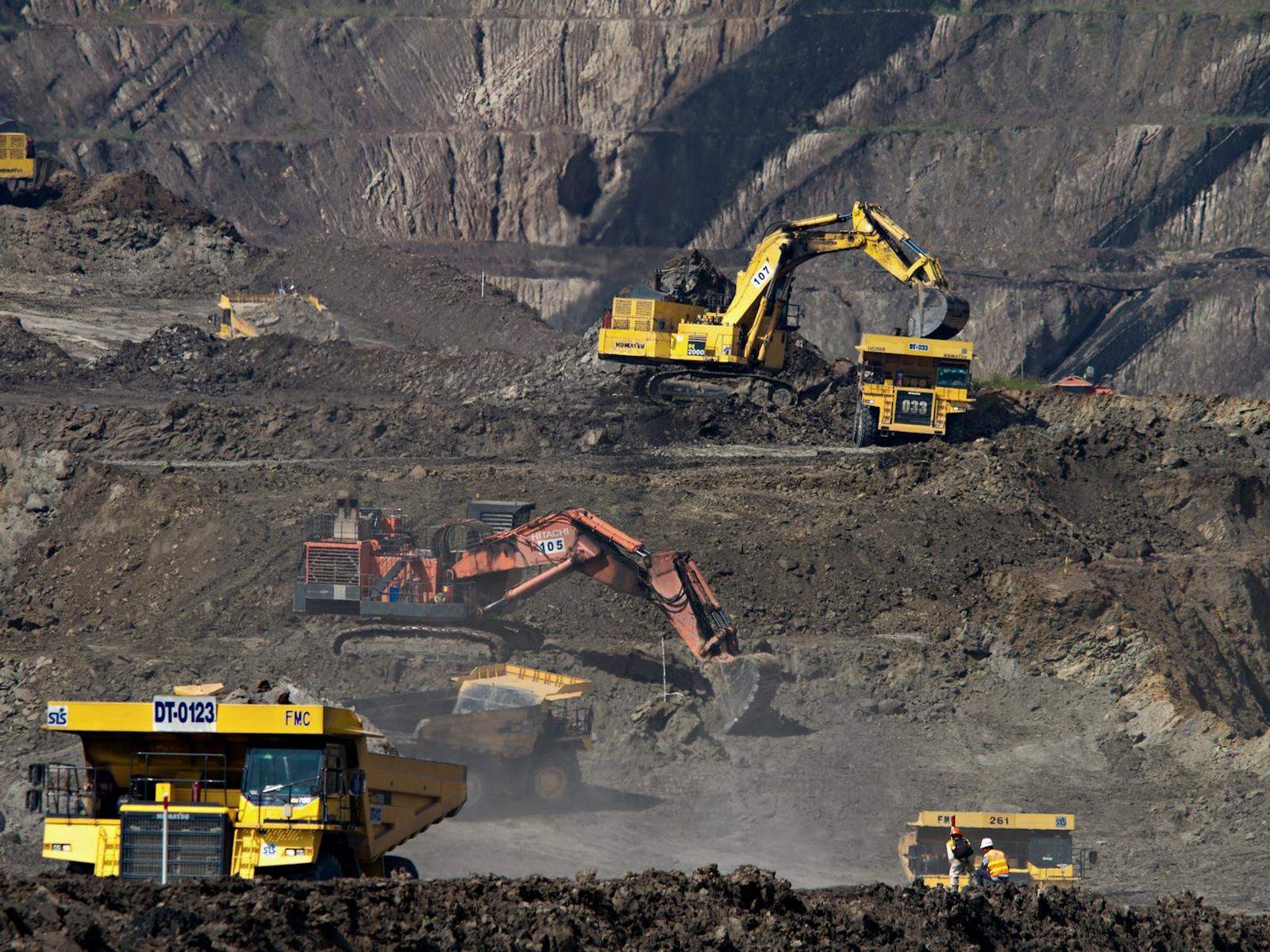 Excavators and haul trucks working an open-pit mine face